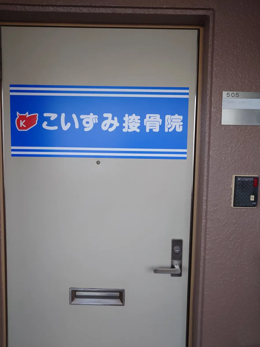 青いこいずみ接骨院の看板と505の部屋番号がある入口の扉